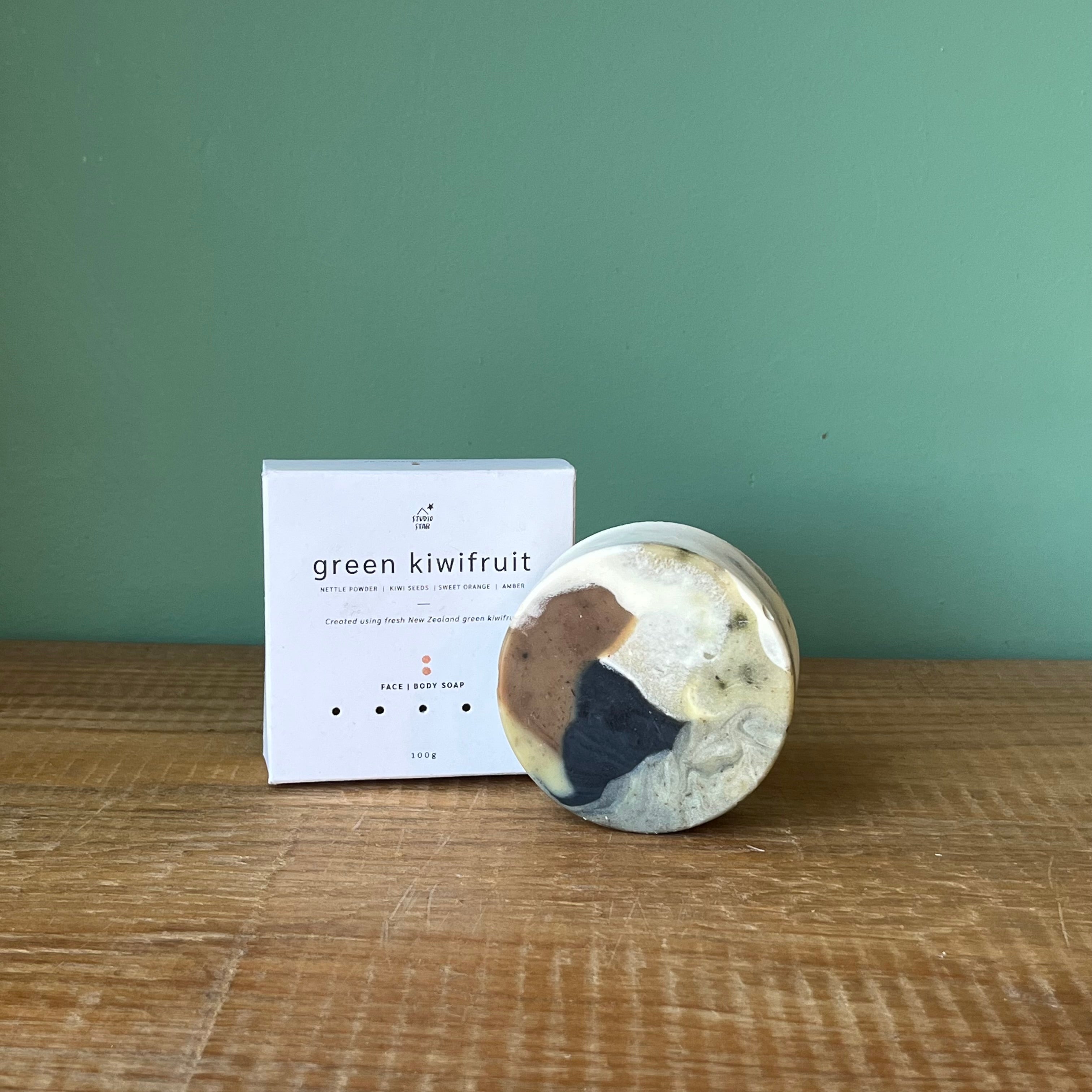 Marbled soap bar with a 'green kiwifruit' packaging on a wooden surface against a green background